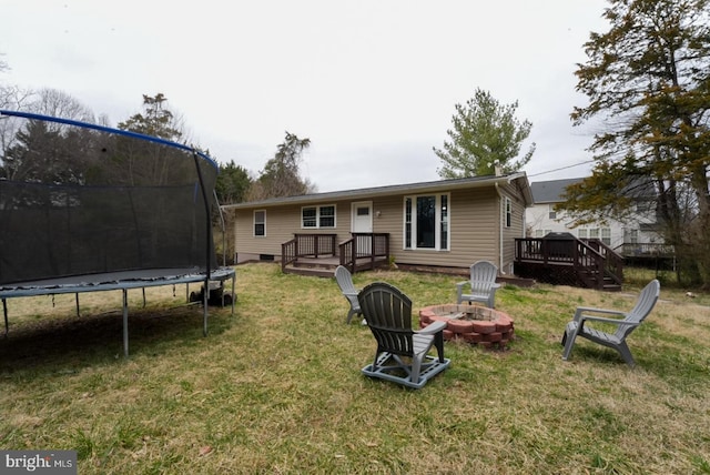 rear view of property featuring a wooden deck, a fire pit, a trampoline, and a yard