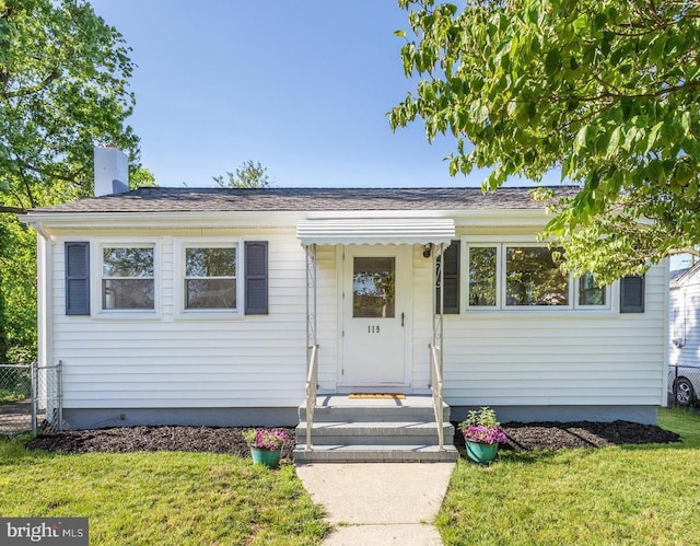 view of front of house with roof with shingles, a chimney, a front lawn, and fence