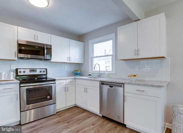 kitchen with a sink, light wood-type flooring, appliances with stainless steel finishes, and white cabinetry