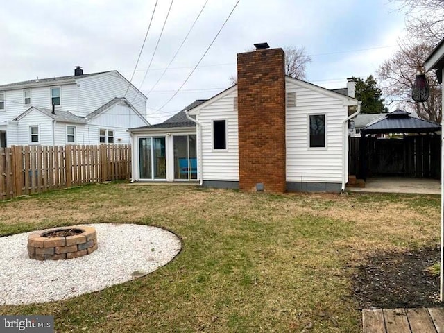 rear view of house featuring a lawn, fence, a gazebo, a fire pit, and a chimney