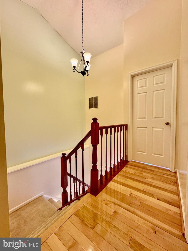 staircase featuring a chandelier, visible vents, vaulted ceiling, and hardwood / wood-style flooring