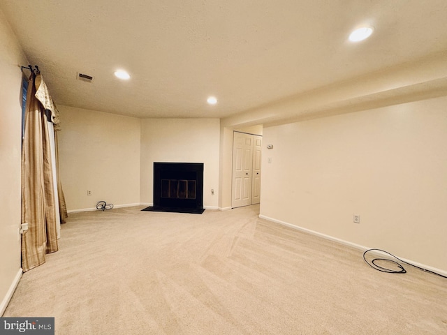 below grade area featuring visible vents, baseboards, a fireplace with flush hearth, recessed lighting, and light colored carpet