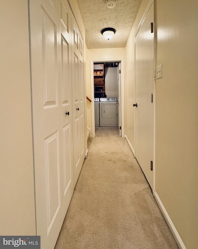 corridor with baseboards, light colored carpet, washing machine and dryer, and a textured ceiling