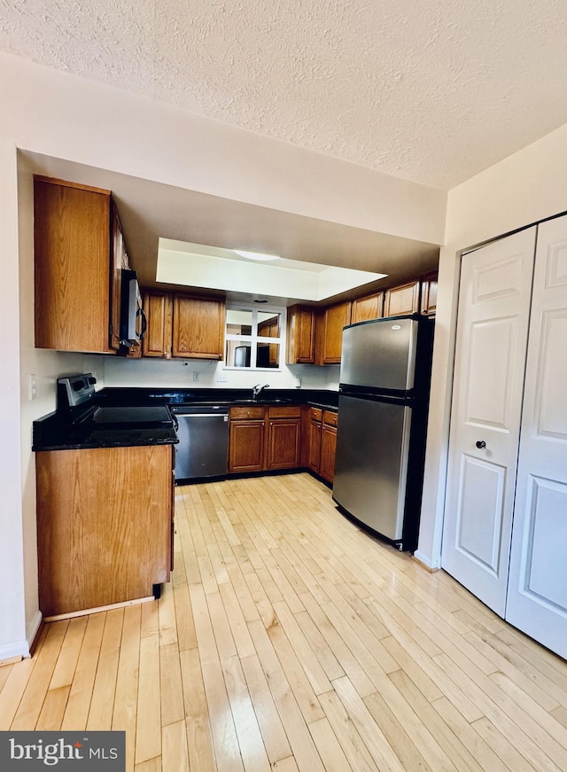 kitchen featuring light wood-style floors, stainless steel appliances, dark countertops, and brown cabinetry