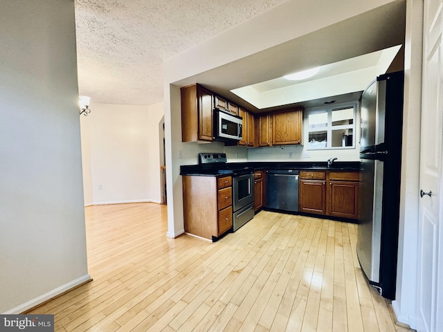 kitchen with a sink, dark countertops, a textured ceiling, stainless steel appliances, and light wood finished floors