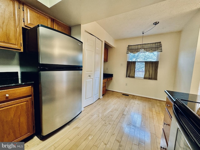 kitchen with brown cabinetry, light wood finished floors, freestanding refrigerator, dark countertops, and decorative light fixtures