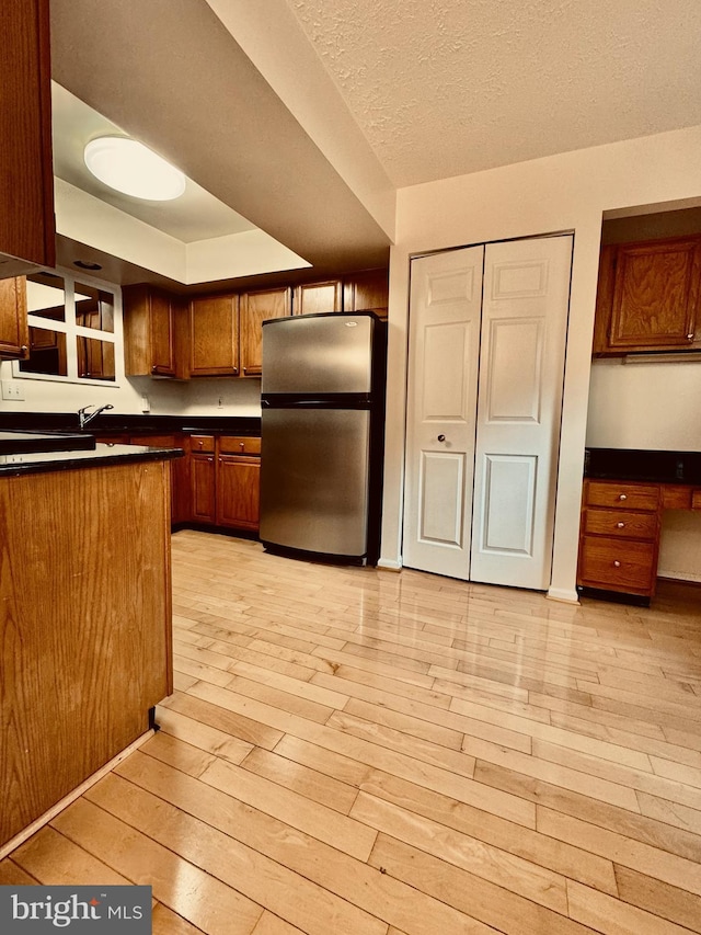 kitchen featuring dark countertops, light wood-style flooring, freestanding refrigerator, and brown cabinets