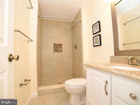 bathroom featuring a textured ceiling, toilet, vanity, and a tile shower