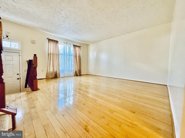 unfurnished room with a wealth of natural light, light wood-type flooring, baseboards, and a textured ceiling