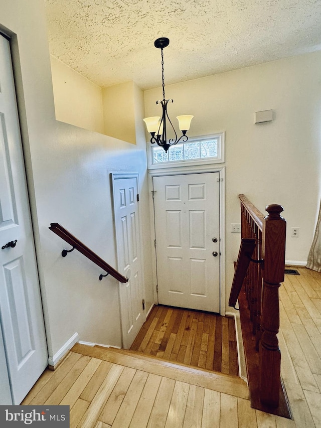 entryway featuring a notable chandelier, a textured ceiling, baseboards, and hardwood / wood-style floors