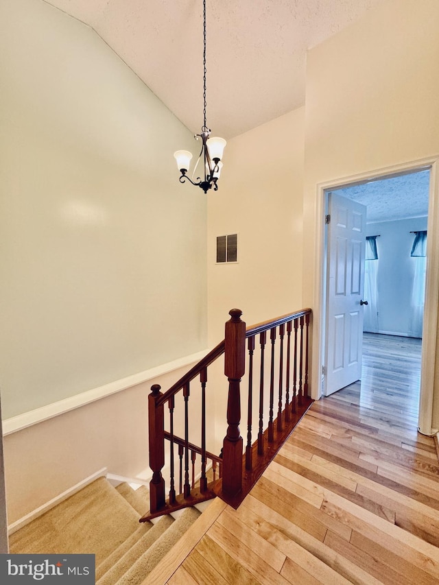 stairway with an inviting chandelier, hardwood / wood-style flooring, visible vents, and a textured ceiling