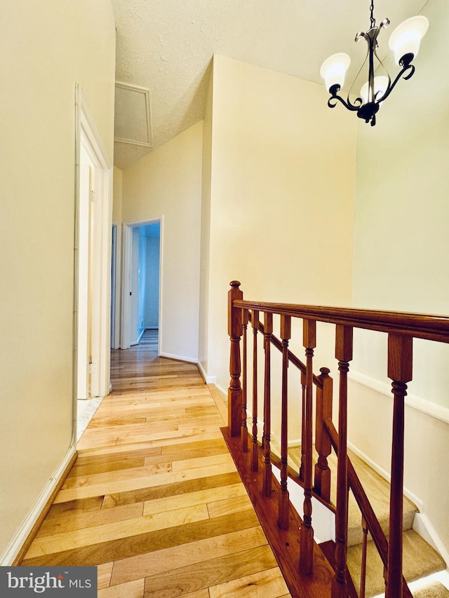 corridor featuring baseboards, a textured ceiling, an inviting chandelier, and hardwood / wood-style floors