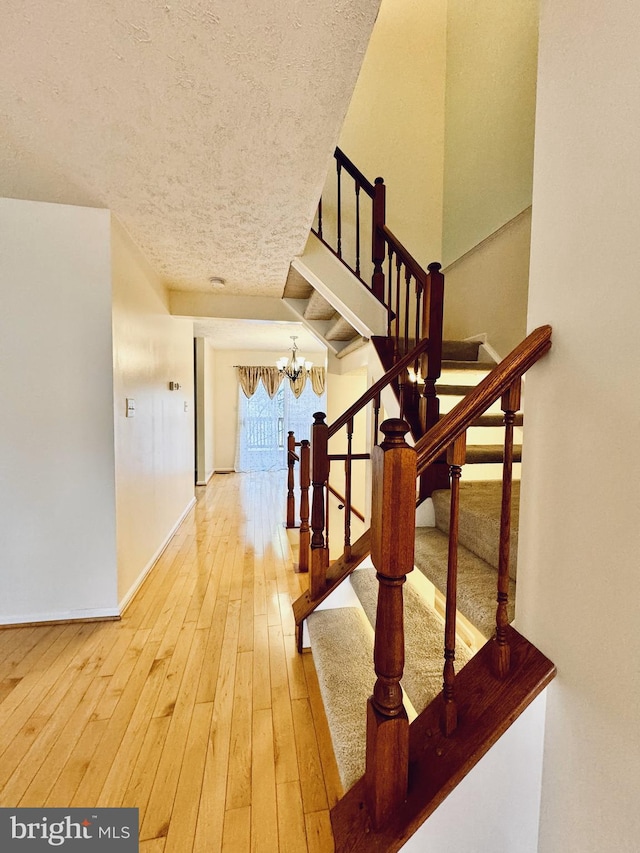 stairway with baseboards, wood-type flooring, a notable chandelier, and a textured ceiling