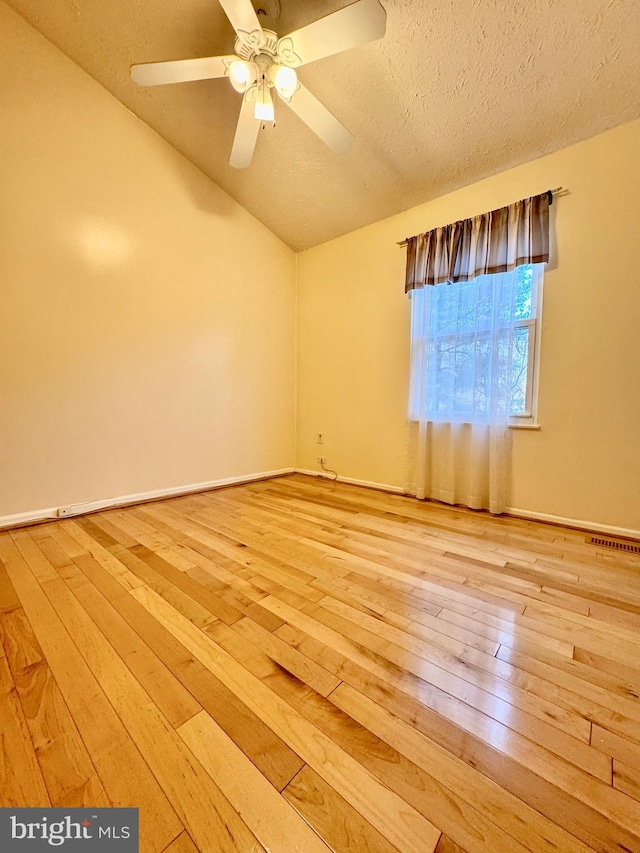 unfurnished room with hardwood / wood-style floors, vaulted ceiling, visible vents, and a textured ceiling