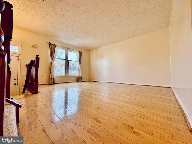 unfurnished room with baseboards, light wood finished floors, and a textured ceiling