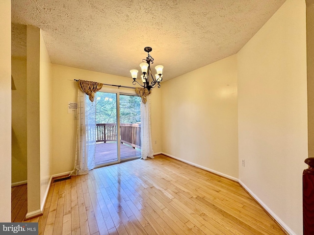 unfurnished dining area featuring a notable chandelier, a textured ceiling, baseboards, and wood-type flooring