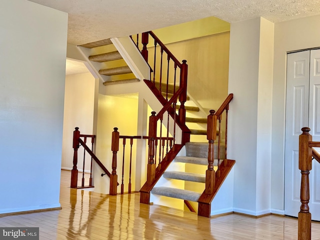 staircase with a textured ceiling, baseboards, and wood-type flooring