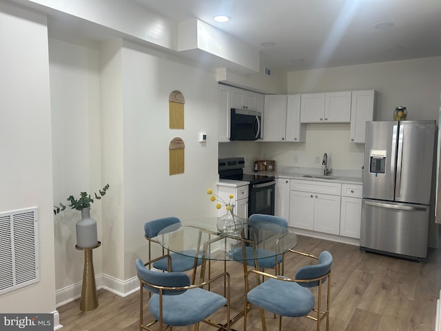 kitchen featuring baseboards, a sink, light countertops, light wood-style floors, and appliances with stainless steel finishes