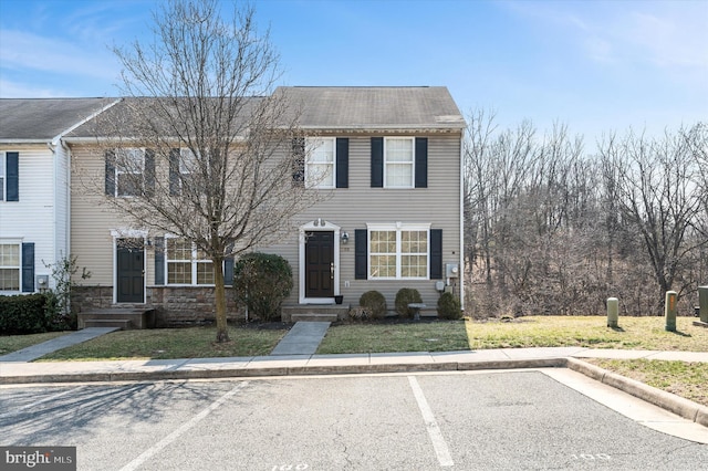 multi unit property featuring stone siding, a front lawn, and uncovered parking