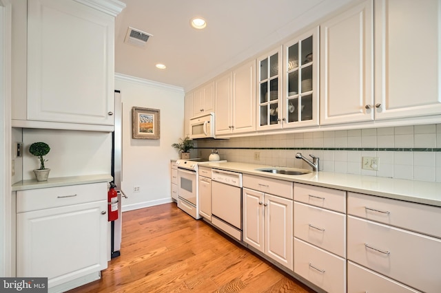 kitchen with white appliances, ornamental molding, decorative backsplash, a sink, and white cabinets