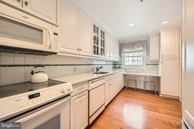 kitchen with white appliances, light wood-style flooring, a sink, decorative backsplash, and white cabinets