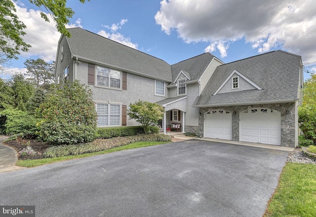 view of front of house featuring driveway, stucco siding, a shingled roof, a garage, and stone siding