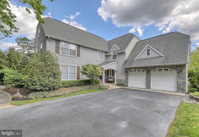 view of front of house with an attached garage, stucco siding, a shingled roof, stone siding, and aphalt driveway