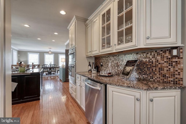 kitchen with tasteful backsplash, glass insert cabinets, ornamental molding, light wood-style floors, and stainless steel appliances