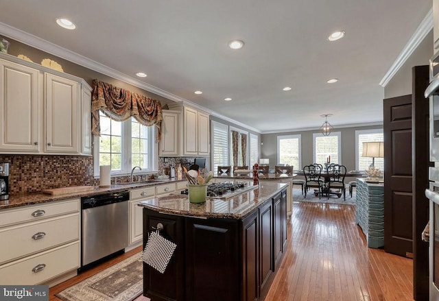 kitchen with tasteful backsplash, ornamental molding, dark stone countertops, light wood-style floors, and stainless steel appliances