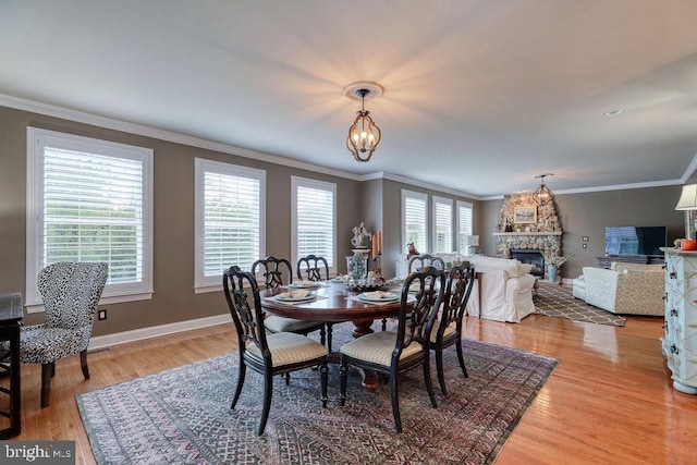 dining area featuring baseboards, a chandelier, ornamental molding, light wood-style flooring, and a fireplace