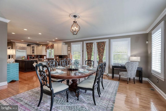 dining area with light wood-style flooring, baseboards, an inviting chandelier, and ornamental molding