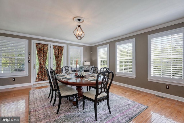 dining area with baseboards, visible vents, light wood-style floors, crown molding, and a notable chandelier