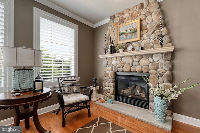 living area featuring a fireplace, crown molding, wood finished floors, and baseboards