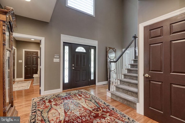 entrance foyer with stairs, a towering ceiling, baseboards, and light wood finished floors