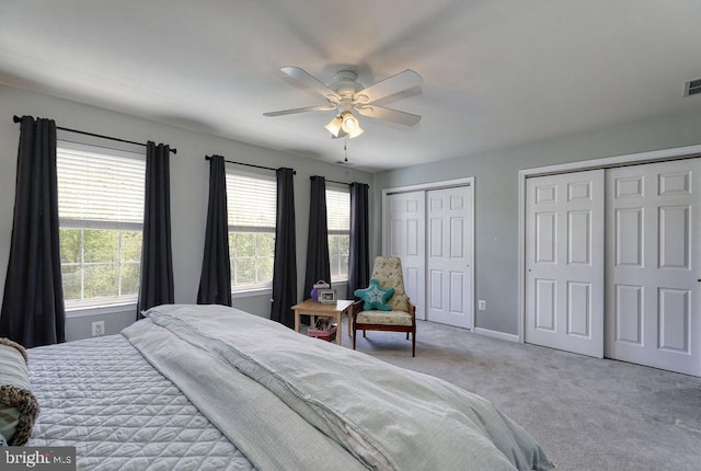 carpeted bedroom featuring visible vents, baseboards, multiple closets, and a ceiling fan