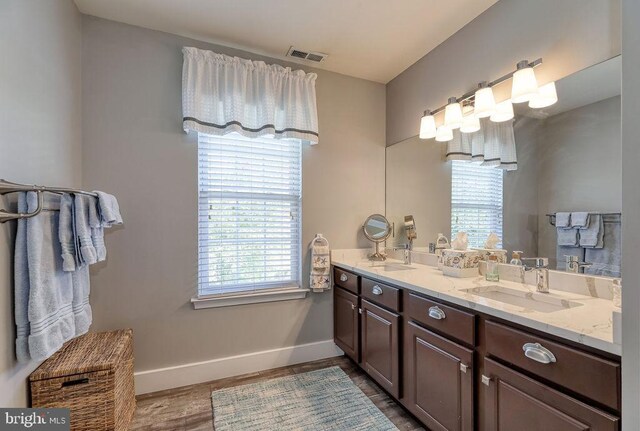 full bath with wood finished floors, baseboards, visible vents, double vanity, and a sink