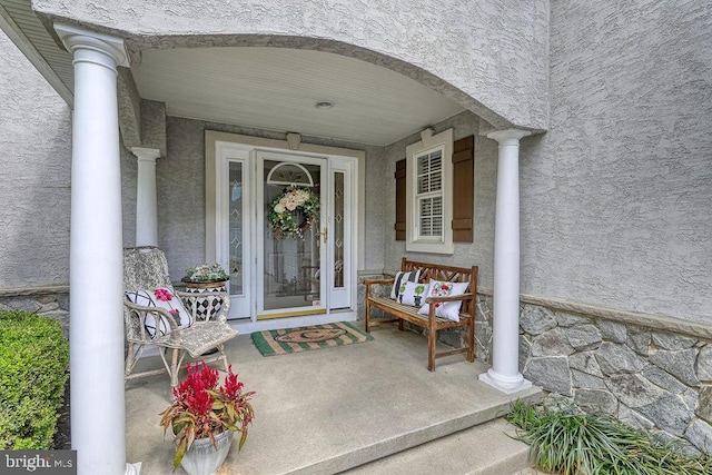 property entrance featuring a porch, stone siding, and stucco siding