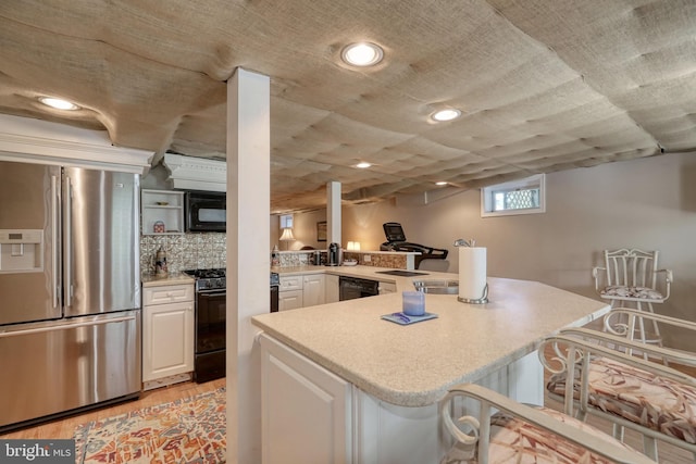 kitchen featuring a peninsula, black appliances, white cabinets, light countertops, and a kitchen bar