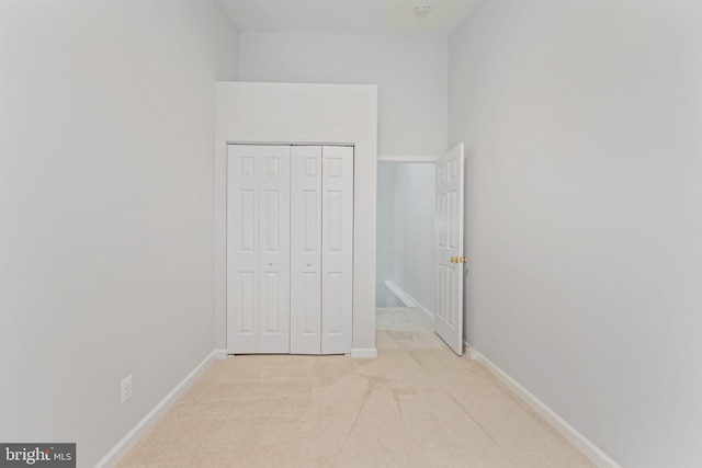 unfurnished bedroom featuring baseboards, a closet, and light carpet