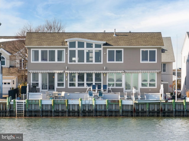 rear view of property with a deck with water view and roof with shingles