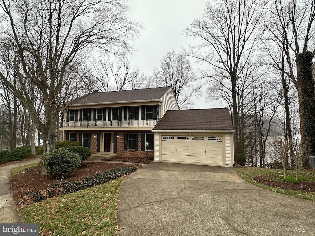 colonial inspired home featuring brick siding, driveway, a shingled roof, and a garage