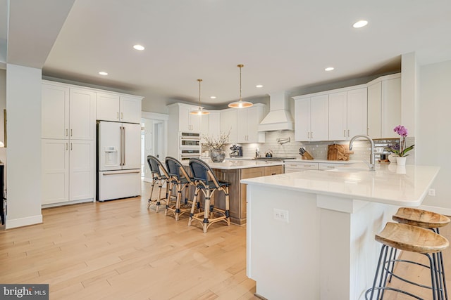 kitchen featuring premium range hood, a sink, a kitchen breakfast bar, white appliances, and light wood-style floors