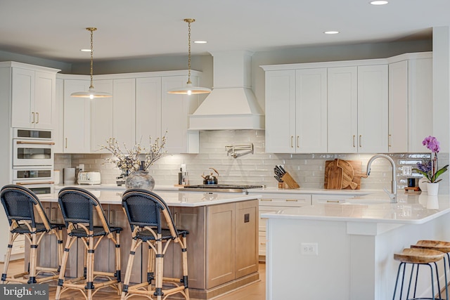 kitchen with a breakfast bar area, stainless steel gas cooktop, custom exhaust hood, a sink, and light countertops