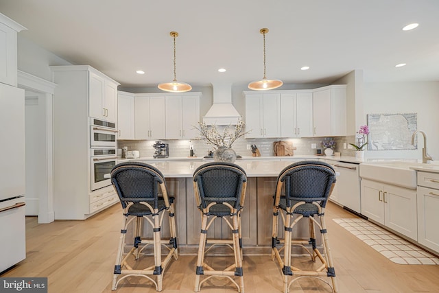 kitchen with white appliances, a sink, light countertops, custom range hood, and white cabinetry