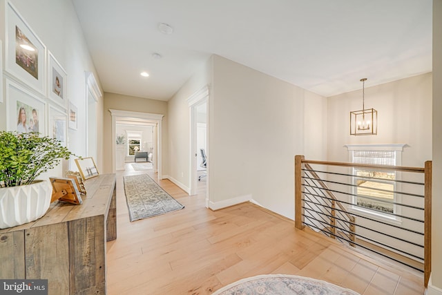 hall with an upstairs landing, light wood-style flooring, recessed lighting, an inviting chandelier, and baseboards