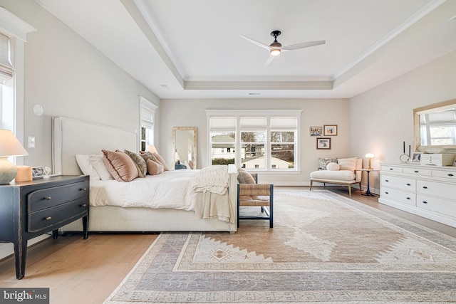 bedroom with a tray ceiling, wood finished floors, visible vents, and ornamental molding