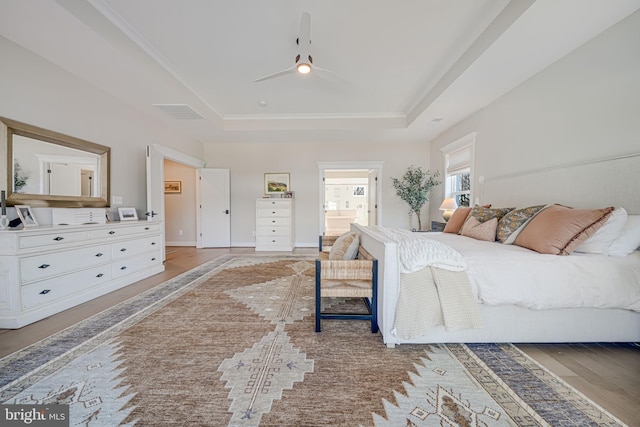 bedroom featuring baseboards, visible vents, ensuite bath, a raised ceiling, and light wood-type flooring