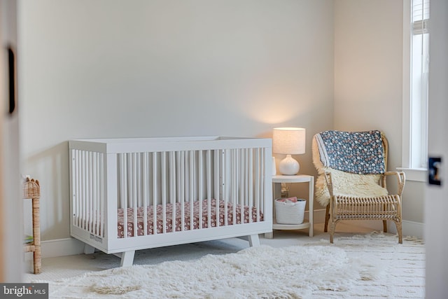 carpeted bedroom featuring a nursery area and baseboards