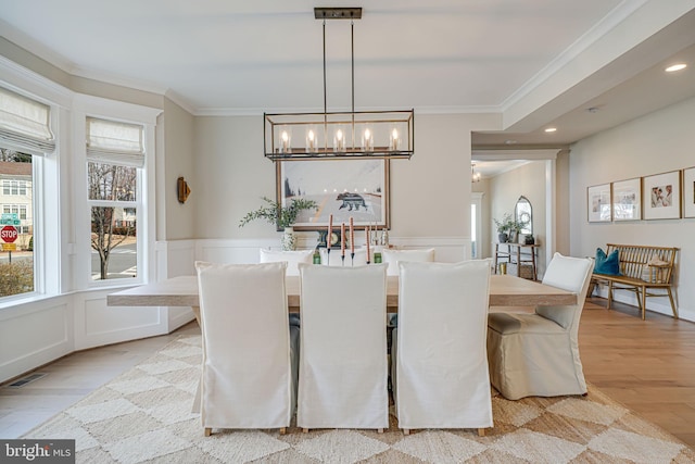 dining space with a wainscoted wall, light wood-type flooring, an inviting chandelier, and ornamental molding