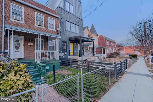 view of front of home featuring a gate, cooling unit, a porch, a fenced front yard, and brick siding